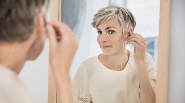 Frau setzt sich Im-Ohr-Hörgerät ins Ohr